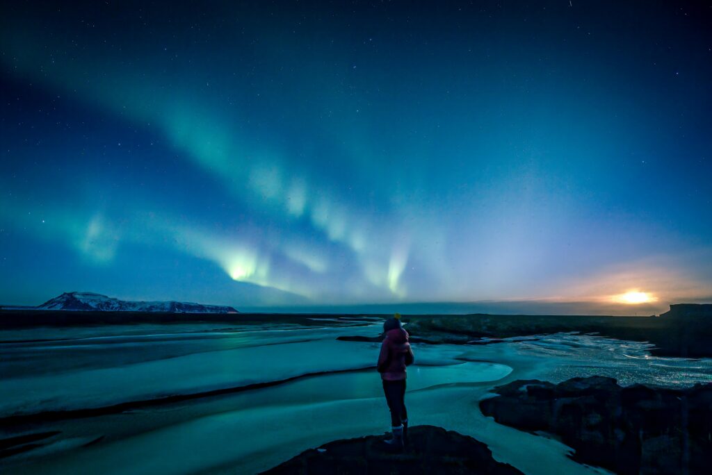 A breathtaking view of the Northern Lights illuminating a frozen Icelandic landscape with a silhouetted figure.